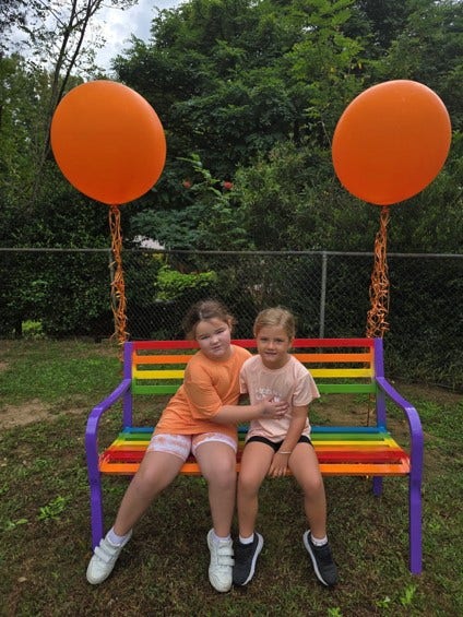 2 girls sitting on a colourful bench with baloons